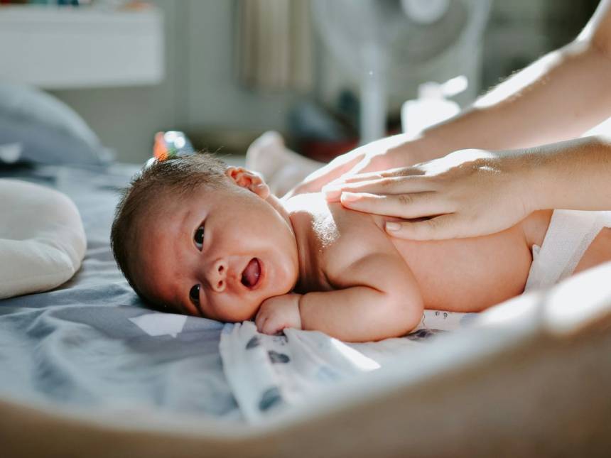 baby laying on bed while woman massaging his back